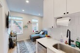 Located at 15 Bartlett Pl in Boston's historic North End, this thoughtfully designed unit maximizes every inch of its single-floor layout across five distinct spaces. The open kitchen features crisp white cabinetry, a stainless steel sink, sleek quartz countertops, and a geometric hexagonal tile backsplash, flowing seamlessly into a bright living area. The living space is warmed by natural light from multiple windows with views of the surrounding brick neighborhood, and is equipped with a wall-mounted mini-split HVAC unit for year-round comfort. Recessed lighting throughout adds a clean, modern touch. Multiple bedrooms offer cozy retreats, each with windows that bring in natural light, and some equipped with individual mini-split units for personalized climate control. The bedrooms provide functional layouts suitable for sleeping and working. A well-appointed bathroom features large-format white subway tile walls, a penny-tile shower floor with a built-in niche, and efficient fixtures. Light hardwood flooring runs through several rooms, complementing the neutral, light-toned walls that give the entire unit a bright and airy feel. This unit offers a practical and modern living experience in one of Boston's most vibrant and walkable neighborhoods.