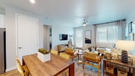 This single-floor residence offers a thoughtfully designed layout with a clean, modern aesthetic carried consistently throughout. The living area is bright and welcoming, featuring wood-look flooring, a ceiling fan, and multiple windows dressed with plantation shutters that allow ample natural light. A wall-mounted TV, comfortable seating arrangement, and direct access to an exterior door make this space both functional and inviting.

The kitchen is finished with white shaker cabinetry, white quartz countertops, and stainless steel appliances including a dishwasher, electric range, and built-in microwave. A window above the sink adds natural light, and a kitchen island provides additional prep space.

The primary bedroom offers a serene retreat with a neutral accent wall, wood-look flooring, and windows with curtains. Its ensuite bathroom features a long dual-sink vanity with white cabinetry, a glass-enclosed shower, and direct access to a generously sized walk-in closet with built-in shelving and hanging rails. A secondary bedroom is cleverly equipped with a built-in Murphy bed and integrated shelving, maximizing flexibility. The second bathroom includes a single vanity and a shower-tub combination with a privacy window above.