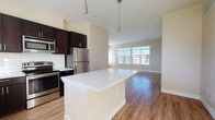 This single-floor residence is designed with a clean, contemporary aesthetic that emphasizes open living and functional design. The heart of the home is an open-concept kitchen and living area, where warm hardwood-style flooring flows seamlessly throughout. The kitchen is well-appointed with dark espresso cabinetry, stainless steel appliances including a refrigerator, range, and built-in microwave, complemented by crisp white subway tile backsplashes and light quartz countertops. A central island with pendant lighting above serves as both a prep space and a natural dividing point between the kitchen and the living area. Large windows in the living space admit generous natural light, creating a bright and welcoming atmosphere.

The bedrooms feature soft wall-to-wall carpeting, ceiling fans, and multiple windows fitted with blinds, providing comfort and natural light. The primary bathroom includes a dual-sink vanity with dark cabinetry, a large mirror, and a tiled tub-shower combination, with an adjacent walk-in closet. A second bathroom mirrors the same refined finishes, featuring a tiled tub-shower surround and hardwood-style flooring. Throughout the unit, neutral tones and consistent finishes create a cohesive and modern living environment.