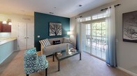 This single-floor residence offers a thoughtfully designed layout across a generous footprint. The living room serves as the heart of the home, featuring plush carpeting, a bold teal accent wall, and sliding glass doors that open to a private balcony with outdoor views, filling the space with natural light. Adjacent areas provide additional flexible living space, ideal for a dining or sitting area, with open sightlines into the hallways and secondary rooms.

The kitchen is well-equipped, featuring rich dark cherry wood cabinetry, light countertops, black appliances including a range and built-in microwave, a double sink, and tile flooring — offering ample storage and workspace for cooking.

The primary bedroom is a serene retreat, highlighted by a large arched window overlooking lush greenery, soft carpet, and generous room for furnishings. The second bedroom also enjoys abundant natural light through multiple windows and is equally well-sized.

Both bathrooms are finished with tile flooring, tub-shower combinations with decorative curtains, dark wood vanities topped with light countertops, and large mirrors. A dedicated in-unit laundry room houses a full-size washer and dryer alongside a water heater, adding everyday convenience to this comfortable and cohesive residence.