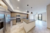 Located at 1050 Blanche St in West Palm Beach, Florida, this modern one-bedroom, one-bathroom residence offers a thoughtfully designed single-floor layout. The open-concept kitchen and dining area serves as the heart of the home, showcasing light wood-grain cabinetry, a grey subway tile backsplash, stainless steel appliances including a refrigerator, range, microwave, and dishwasher, and a large central island with a dark quartz countertop. Stylish pendant lights hang above the island, complementing the recessed lighting throughout. Light-toned tile flooring flows through the main living areas, adding a clean, contemporary feel. The living room connects seamlessly to a private balcony through glass-paneled doors, offering outdoor views of the surrounding West Palm Beach neighborhood framed by tropical palm foliage. The bedroom features soft carpeting, a ceiling fan, and a bright window that invites natural light. Generous closet space is provided across three closets, including a walk-in with wire shelving. Additional conveniences include an in-unit laundry area. The overall ambiance is clean, modern, and move-in ready, reflecting a contemporary Florida aesthetic.