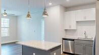 Located on Dr. Martin Luther King Jr. Blvd in New Bern, NC, this thoughtfully laid-out 2-bedroom, 2-bathroom residence offers a clean, modern aesthetic throughout its single floor. The kitchen is a standout feature, showcasing granite countertops on both the island and perimeter surfaces, two-tone cabinetry with white upper cabinets and gray lower cabinets, a white subway tile backsplash, and a full suite of stainless steel appliances including a range, microwave, and dishwasher. Stylish pendant lighting above the island adds a contemporary touch. The living area benefits from wood-look flooring and access to an outdoor balcony through a glass door, allowing for natural light and outdoor views. Both bedrooms are carpeted and equipped with ceiling fans, and each features windows that overlook the surrounding community. The primary bedroom is generously sized and includes a dedicated closet with wire shelving for organized storage. The two bathrooms are finished with granite-topped gray vanities; one includes a walk-in shower and the other a full soaking tub. A dedicated in-unit laundry room accommodates a full-size washer and dryer with additional overhead shelving. Two hallways connect the layout efficiently, completing this well-appointed residence.