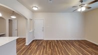 This single-story unit offers a thoughtfully designed layout with a consistent neutral color palette of warm beige tones and crisp white trim throughout. The main living and dining areas feature durable wood-look plank flooring, ceiling fans with integrated lighting, and access to an exterior door flanked by windows fitted with blinds, allowing natural light to fill the space.

The kitchen is well-equipped with dark espresso cabinetry, granite-style countertops, a double-basin stainless steel sink, and a full suite of stainless steel appliances including a refrigerator, electric range, and built-in microwave. Track lighting overhead ensures ample illumination, and the layout provides generous counter and storage space along both sides of the galley-style configuration.

The bedrooms are carpeted and each include ceiling fans, with windows providing natural light. The bathrooms feature dark wood vanities with granite-style countertops, large mirrors, tile flooring, and tub/shower combinations with tiled surrounds. One bathroom includes additional wall-mounted cabinetry for storage. A dedicated in-unit laundry area accommodates a full-size washer and dryer with overhead wire shelving for added utility.