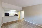 This single-floor residence offers a clean, functional layout designed for comfortable everyday living. The open-concept living area is finished with light wood-style flooring and neutral gray walls, creating a bright and welcoming atmosphere. A textured ceiling adds subtle character throughout the main living space, which flows seamlessly toward the front entry door framed by a window that invites natural light.

The kitchen is positioned adjacent to the living area and features white cabinetry with brushed nickel hardware, light granite-style countertops, and black appliances including a refrigerator, range, and dishwasher. A skylight panel above the kitchen provides additional illumination, and a breakfast bar separates the kitchen from the main living space, enhancing the open feel.

The bedroom is carpeted for comfort and includes a ceiling fan with light fixture and a window fitted with blinds, allowing for natural light and ventilation. The full bathroom is finished with wood-style flooring, a white vanity with cabinet storage, and a tub-shower combination, maintaining the home's clean and consistent aesthetic.

A dedicated utility room houses the water heater and electrical panel, providing practical infrastructure in a neatly organized space. Throughout the residence, consistent flooring, neutral tones, and thoughtful finishes contribute to a cohesive and move-in-ready environment.