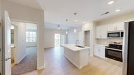 Located at 1001 Victory Lap Ln in Holly Ridge, NC, this well-designed single-floor home offers three bedrooms, two bathrooms, and a thoughtfully organized layout. The open-concept kitchen serves as the heart of the home, showcasing white shaker cabinetry, quartz countertops, a center island with an undermount sink and pendant lighting, and a full suite of stainless steel appliances including a French door refrigerator, range, microwave, and dishwasher. Light hardwood-style flooring flows through the kitchen and living areas, creating a bright, cohesive aesthetic. The living area extends toward a balcony door, allowing natural light to fill the space, and is equipped with a ceiling fan. The spacious primary bedroom features plush carpeting and a ceiling fan, while the additional bedrooms also offer carpet, ceiling fans, natural light from large windows, and closet space. The primary bathroom includes a walk-in shower with a glass door and a vanity with ample cabinetry, while the second bathroom features a full tub-shower combination. A dedicated laundry room houses a full-size washer and dryer with overhead wire shelving for added storage. Three closets throughout the home provide generous organizational capacity.