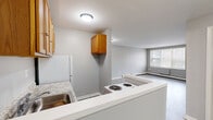 Located at 887 Asylum Ave in Hartford, CT, this two-bedroom, one-bathroom unit offers a practical and well-organized single-floor layout. The open-concept kitchen flows directly into the living area, creating a connected and functional common space. The kitchen features warm-toned wood cabinetry, a coil-top electric range, a white refrigerator, a stainless sink with granite-style countertops, and a pass-through counter that defines the transition into the living area. The living room benefits from a large multi-pane window that brings in natural light and views of the surrounding neighborhood.

Both bedrooms feature light wood-style laminate flooring, neutral gray walls, and baseboard heating units. The spacious primary bedroom includes a sliding-door closet with built-in shelving and direct access to the kitchen area. The second bedroom also features a window for natural light, providing a comfortable and airy feel.

The bathroom is clean and efficiently designed, with a white vanity cabinet topped by a mirrored medicine cabinet, and a full-sized soaking tub with an overhead shower. Light tile flooring completes the space. Throughout the unit, consistent neutral tones and low-maintenance finishes contribute to a clean, move-in ready environment.