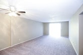 This single-story residence offers a practical and straightforward layout across several well-defined rooms. The kitchen is equipped with white cabinetry extending to the ceiling, a tile backsplash, laminate wood-style flooring, a double-basin sink, a gas range, a built-in microwave, and a dishwasher, providing ample storage and functionality for everyday cooking.

The living area is generously sized, featuring neutral-toned carpet, a ceiling fan with light fixture, and a large sliding glass door dressed with vertical blinds that allows natural light to fill the room. The textured popcorn ceiling is consistent throughout the living and bedroom spaces.

Multiple bedrooms are present, each carpeted and painted in warm neutral tones. The bedrooms are served by windows that bring in natural light and feature closets, with some offering walk-in or open-shelf closet configurations.

The bathrooms include a full tub and shower combination with white tile surround and wood-style flooring, as well as a vanity area with a granite-look countertop, white cabinetry, a large mirror, and bar lighting. The overall ambiance is clean, neutral, and move-in ready.