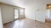 This single-story apartment at Woods Edge Apartment Homes in Muncie, Indiana, offers a practical and comfortable layout with a neutral color palette throughout. The living area features light wood-look flooring, a textured ceiling, and a glass door paired with an adjacent window that allows natural light to pour in, creating a bright and open atmosphere. A dedicated entryway with a paneled front door provides a welcoming transition into the main living space.

The kitchen is efficiently arranged with white cabinetry, laminate countertops, and black appliances, including a refrigerator and range. A window above the kitchen area brings in additional natural light, while the wood-look flooring continues seamlessly from the main living areas. The layout allows for easy flow between the kitchen and adjacent spaces.

The bedrooms feature neutral carpet flooring and individual windows fitted with blinds, providing both comfort and natural light. Each room offers a clean, versatile space suitable for various furniture arrangements.

The bathroom includes a full tub and shower combination with a curtain rod, a vanity with storage, and wood-look flooring, maintaining the cohesive design found throughout the unit. Overall, the space presents a clean, functional living environment with consistent finishes.