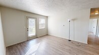 This single-story apartment at Woods Edge Apartment Homes in Muncie, Indiana, offers a practical and comfortable layout with a neutral color palette throughout. The living area features light wood-look flooring, a textured ceiling, and a glass door paired with an adjacent window that allows natural light to pour in, creating a bright and open atmosphere. A dedicated entryway with a paneled front door provides a welcoming transition into the main living space.

The kitchen is efficiently arranged with white cabinetry, laminate countertops, and black appliances, including a refrigerator and range. A window above the kitchen area brings in additional natural light, while the wood-look flooring continues seamlessly from the main living areas. The layout allows for easy flow between the kitchen and adjacent spaces.

The bedrooms feature neutral carpet flooring and individual windows fitted with blinds, providing both comfort and natural light. Each room offers a clean, versatile space suitable for various furniture arrangements.

The bathroom includes a full tub and shower combination with a curtain rod, a vanity with storage, and wood-look flooring, maintaining the cohesive design found throughout the unit. Overall, the space presents a clean, functional living environment with consistent finishes.