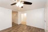 This single-story unit located along US-62 in Lubbock, Texas, offers a straightforward and functional layout across several connected rooms. The main living area features warm wood-look plank flooring and white walls, creating a bright, clean atmosphere. A ceiling fan with a light fixture provides overhead comfort, while a wall-mounted PTAC unit ensures climate control. Natural light filters in through a window with horizontal blinds, adding a welcoming feel to the space.

The layout transitions through an open passage into a carpeted bedroom area, where built-in white cabinetry lines one wall, offering generous storage. A ceiling fan is installed here as well, maintaining consistent comfort throughout. An additional carpeted room, also with a ceiling fan and light fixture, provides flexible use as a bedroom or secondary space.

The kitchen is equipped with white cabinetry above and below the countertops, a double stainless steel sink beneath a window, and a white electric coil-top range with a vent hood above. Light tile flooring runs through this area, complementing the neutral color scheme.

The bathroom includes a wide vanity with a speckled composite countertop, an integrated white basin, chrome fixtures, and a large mirror with overhead lighting. A tiled shower area is visible in the mirror's reflection, completing the bathroom's practical design.