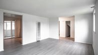 This two-floor residence at 2111 Newton Rd in Hampton, Virginia offers a practical and well-organized layout across multiple levels. The main living area is spacious and open, finished with light-toned laminate wood flooring that extends throughout the common spaces. White walls and a textured ceiling contribute to a clean, neutral aesthetic, while a wall-mounted heating unit provides efficient climate control. A sliding glass door connects the living area to an outdoor space, allowing natural light to flow into the room.

The kitchen is positioned adjacent to the living area and features warm-toned wood cabinetry with ample upper and lower storage. Black appliances, including a gas range, dishwasher, and refrigerator, are complemented by granite-style countertops and a single-basin sink. A range hood and built-in ventilation grilles are also present.

The bedrooms are carpeted and offer a quieter, softer feel. Each room includes a closet with a rod and shelf system, and select bedrooms feature windows that bring in natural light and outdoor views. The bathroom includes a full tub-shower combination with built-in shelving and a small window above for ventilation and light.