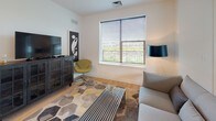 Located at 3575 Silverside Rd in Wilmington, Delaware, this contemporary single-floor residence offers a thoughtfully designed layout with modern finishes throughout. Light wood flooring flows seamlessly across the entire space, creating a warm and cohesive aesthetic.

The open-concept living area is anchored by large windows fitted with horizontal blinds, allowing ample natural light and outdoor views of the surrounding greenery. The space accommodates a comfortable seating arrangement alongside a media console, giving the room a functional yet refined character.

The kitchen features a galley-style design with dark lower cabinetry contrasted by white countertops, stainless steel appliances including a full-size refrigerator, dishwasher, and range, along with pendant lighting above the countertop island. An adjacent dining area with large windows brings in additional natural light.

The residence includes multiple bedrooms, each featuring large windows, closet storage, and clean white walls that lend a bright, airy feel. Framed artwork adds a curated touch to each room.

Two bathrooms echo the modern design language of the home, each featuring floating wood vanities with white countertops, large mirrors, and continued light wood flooring. The clean, minimalist aesthetic is consistent throughout, making this a well-appointed and contemporary living space.