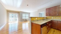 This single-floor residence is thoughtfully designed with an open-concept layout that seamlessly connects the kitchen and living area. The kitchen is well-equipped with rich cherry wood cabinetry, granite countertops, a golden mosaic tile backsplash, and a full suite of stainless steel appliances, including a refrigerator, range, and dishwasher. A peninsula with a built-in sink provides additional prep space and visual separation from the living area. The living space features warm hardwood flooring that extends throughout, neutral gray walls, and generous natural light from multiple windows and a sliding glass door leading to a private balcony. The spacious bedroom is carpeted, features a wall-mounted HVAC unit, and connects to a large walk-in closet outfitted with wire shelving for ample storage. Two full bathrooms are finished with tile flooring, cherry vanities with granite countertops, and tub-shower combinations featuring tile surrounds. A dedicated laundry area houses a stacked washer and dryer alongside a water heater, adding functional convenience to the overall floor plan.
