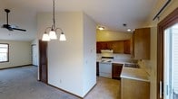 This single-floor space showcases an open and functional layout connecting the dining area to the kitchen. The dining area is highlighted by a classic wrought-iron chandelier with three bell-shaped frosted glass shades, adding a traditional touch to the space. A louvered bifold door is visible nearby, likely concealing a closet and contributing a warm, wood-toned accent to the room.

The kitchen is positioned adjacent to the dining area and features warm medium-toned wood cabinetry along both the upper and lower sections, providing ample storage. A white electric range with a ventilation hood serves as the cooking centerpiece, flanked by generous counter space. A built-in sink with a single-handle faucet is integrated into the peninsula counter, which also doubles as a natural divider between the kitchen and dining spaces.

The flooring transitions from carpet in the dining area to a hard surface in the kitchen. Recessed and flush-mount ceiling lighting illuminates the kitchen, while neutral-toned walls and light-colored countertops keep the overall atmosphere clean and understated. The layout emphasizes practicality and ease of movement throughout the space.