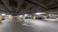 This single-floor property offers 4 bedrooms and 2 bathrooms. A notable feature is the covered parking facility visible in the provided image. The parking structure is a multi-bay, indoor garage characterized by a concrete overhead ceiling supported by bold yellow-painted columns that provide clear visual markers throughout the space. The floor is finished in smooth concrete, painted with white directional arrows and clearly delineated parking stall lines to ensure organized vehicle flow and easy navigation. Overhead fluorescent lighting illuminates the area evenly, making the space functional during all hours. The exposed ceiling reveals structural beams and utility conduits, reflecting a utilitarian architectural approach typical of purpose-built parking facilities. Multiple parking bays are visible, with vehicles currently occupying several stalls, demonstrating the garage's practical capacity. The structure's design prioritizes efficiency and accessibility, providing residents or guests with a secure and sheltered parking option. Overall, the parking facility adds a layer of convenience to this 4-bedroom, 2-bathroom property, offering protected vehicle storage in a well-organized, clearly navigable environment.