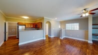 This two-floor home offers a thoughtfully designed layout that balances open living spaces with functional private areas. The main level showcases rich hardwood flooring throughout, complemented by neutral gray walls, crown molding, and clean white baseboards that lend a polished, cohesive aesthetic. The open-concept living area flows seamlessly into a kitchen separated by a half-wall breakfast bar, where warm honey-toned wood cabinetry pairs with stainless steel appliances, including a refrigerator, range, and built-in microwave. A graceful arched doorway adds architectural character to the living space, which also benefits from natural light through large windows. Upstairs, the layout includes a generously sized bonus room or loft area with gleaming hardwood floors, a ceiling fan, built-in shelving, and multiple windows that invite ample natural light and outdoor views. Carpeted bedrooms provide a comfortable retreat, with one featuring a ceiling fan and a bright window overlooking greenery. A walk-in closet with wire shelving offers practical storage. The full bathroom is well-appointed with a combined tub and shower, a vanity with storage, and hardwood flooring. An attached garage with a concrete floor and automatic opener rounds out this functional and inviting home.
