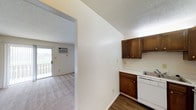 Located at 700 Saint Marys Ave in Frankfort, Indiana, this single-floor unit offers a straightforward and functional layout designed for comfortable everyday living. The kitchen features rich, dark wood cabinetry providing ample storage, light countertops, and a white dishwasher, with durable wood-style flooring underfoot that adds a warm, practical touch. A textured ceiling runs throughout, giving the space a classic residential character. Adjacent to the kitchen, a wide open passage leads into the carpeted living area, which is finished with neutral tones that create a clean and inviting atmosphere. The living space is equipped with a wall-mounted air conditioning unit, ensuring year-round comfort. A sliding glass door fills the room with natural light and provides direct access to an outdoor balcony, offering views of the surrounding exterior — a notable feature that enhances the sense of openness. The overall layout is efficient and well-connected, making it easy to move between the kitchen and living areas. With its practical finishes, natural light, and outdoor access, this unit presents a functional and livable space in a residential Frankfort neighborhood.