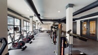Located at 950 Riverside Dr in Chattanooga, Tennessee, this well-appointed fitness center offers a comprehensive workout environment across a single, expansive floor. The space is defined by its industrial-chic aesthetic, showcasing exposed black ductwork running along the ceilings, white structural columns with charcoal accent details, and durable rubber flooring throughout — combining style with functionality.

The main workout area is generously sized and lined with large windows that invite abundant natural light and outdoor views, creating an energizing atmosphere. A full row of treadmills and elliptical machines is positioned along the windowed wall, while rowing machines and cable systems occupy the open central floor. A dedicated strength-training zone features a multi-rack dumbbell station, a weight bench, and a cable/functional trainer machine, providing a complete resistance training setup.

A separate studio room with cork flooring offers space for group fitness, stretching, or functional training, and is equipped with stability balls, resistance bands, and wall-mounted mirrors. A built-in water fountain station is conveniently accessible within the facility. The overall ambiance is clean, modern, and professional, making this fitness center a well-rounded facility suited for a wide range of training goals.