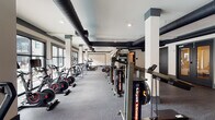 Located at 950 Riverside Dr in Chattanooga, Tennessee, this well-appointed fitness center offers a comprehensive workout environment across a single, expansive floor. The space is defined by its industrial-chic aesthetic, showcasing exposed black ductwork running along the ceilings, white structural columns with charcoal accent details, and durable rubber flooring throughout — combining style with functionality.

The main workout area is generously sized and lined with large windows that invite abundant natural light and outdoor views, creating an energizing atmosphere. A full row of treadmills and elliptical machines is positioned along the windowed wall, while rowing machines and cable systems occupy the open central floor. A dedicated strength-training zone features a multi-rack dumbbell station, a weight bench, and a cable/functional trainer machine, providing a complete resistance training setup.

A separate studio room with cork flooring offers space for group fitness, stretching, or functional training, and is equipped with stability balls, resistance bands, and wall-mounted mirrors. A built-in water fountain station is conveniently accessible within the facility. The overall ambiance is clean, modern, and professional, making this fitness center a well-rounded facility suited for a wide range of training goals.