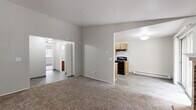 Located at 9887 Enterprise Ln NW in Silverdale, Washington, this single-floor unit offers a practical and well-organized layout across several distinct living areas. The kitchen is equipped with warm wood-toned cabinetry, granite-style countertops, a double-basin sink, a dishwasher, and black appliances including an electric range and refrigerator. Wood-look vinyl flooring runs throughout the kitchen and extends into adjacent areas, lending a cohesive, easy-to-maintain feel. The living area is generously sized, featuring neutral-toned carpet and open sightlines into both the kitchen and bedroom spaces, creating a connected and airy atmosphere. A baseboard heating unit ensures comfort year-round. The bedroom is carpeted and bathed in natural light from a window overlooking the outdoors, providing a calm and restful environment. A closet with built-in shelving and a hanging rod offers organized storage just steps from the bathroom. The full bathroom is finished with rich dark wood cabinetry, granite-style countertops, light wood-look vinyl flooring, and a full tub and shower combination. The overall design is clean and neutral, with light gray walls throughout, creating a move-in-ready space well suited for comfortable daily living.