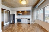 Located at 4501 Ford Ave in Alexandria, Virginia, this two-bedroom, one-bathroom unit showcases an industrial-chic aesthetic that blends raw architectural character with modern finishes. The open-plan living, dining, and kitchen area serves as the heart of the unit, featuring striking exposed concrete ceilings, visible ductwork, and concrete column accents that lend an urban loft feel. Warm hardwood-style flooring runs throughout, complementing the space's contemporary design. Large windows allow natural light to pour in and offer views of the surrounding neighborhood.

The kitchen is well-appointed with stainless steel appliances — including a full-size refrigerator, electric range, microwave, and dishwasher — paired with a two-tone cabinet scheme of white lower and rich dark-wood upper cabinetry, and a clean white tile backsplash.

A bright hallway with recessed lighting connects the main living area to the private quarters. The primary bedroom includes a dedicated closet with built-in shelving and hanging rods. The bathroom features a soaking tub with full-height neutral tile surround. Additional conveniences include an in-unit laundry area and a utility room. Frosted glass partitions add a refined architectural touch to the corridor.