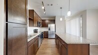 Located in Lone Tree, CO, this well-designed one-bedroom, one-bathroom residence offers a thoughtful layout across a single floor. The open-concept kitchen serves as the heart of the home, showcasing rich dark wood cabinetry, granite countertops, a center island with pendant lighting, stainless steel appliances including a refrigerator, range, and microwave, and a tile backsplash. Warm hardwood-style flooring flows throughout the kitchen and living areas, complemented by track lighting that enhances the bright, airy atmosphere. The bedroom is a comfortable retreat featuring plush carpeting, neutral-toned walls, and a ceiling fan. Natural light filters in through a large window fitted with blinds, offering views of the surrounding neighborhood. A dedicated walk-in closet provides generous storage with wire shelving and hanging rods across multiple levels. The bathroom is finished with a dual-sink vanity topped with granite, dark wood cabinetry, a tiled shower-tub combination, and wood-look tile flooring. A hallway connects the living spaces efficiently, completing this clean and functional floor plan ideal for those seeking comfortable, low-maintenance living in the Lone Tree area.