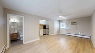 Located at 2837 Minto Ave in Cincinnati's 45208 zip code, this efficiently designed single-floor unit offers a thoughtful layout that maximizes every square foot. The open living area features light-toned luxury vinyl plank flooring throughout, neutral beige walls, and a ceiling fan with integrated lighting that enhances air circulation and ambiance. Baseboard heating units run along the perimeter walls, ensuring consistent warmth. Natural light filters in through windows fitted with white blinds, lending the space a bright and airy feel. A wall-mounted air conditioning unit provides additional climate control. The kitchen is neatly integrated into the main living space and is equipped with white shaker-style cabinetry, a textured tile backsplash, a stainless steel refrigerator, a dishwasher, and a sink — all designed for functional, everyday use. A closet provides dedicated storage. The bathroom is a standout feature, showcasing modern finishes including a floating wood-toned vanity with a white rectangular sink, brass hardware accents, a lighted mirror, floor-to-ceiling subway tile surrounding a soaking tub, and slate-toned floor tile. The overall aesthetic is clean, modern, and move-in ready, making this Cincinnati unit a practical and stylish space.