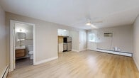 Located at 2837 Minto Ave in Cincinnati's 45208 zip code, this efficiently designed single-floor unit offers a thoughtful layout that maximizes every square foot. The open living area features light-toned luxury vinyl plank flooring throughout, neutral beige walls, and a ceiling fan with integrated lighting that enhances air circulation and ambiance. Baseboard heating units run along the perimeter walls, ensuring consistent warmth. Natural light filters in through windows fitted with white blinds, lending the space a bright and airy feel. A wall-mounted air conditioning unit provides additional climate control. The kitchen is neatly integrated into the main living space and is equipped with white shaker-style cabinetry, a textured tile backsplash, a stainless steel refrigerator, a dishwasher, and a sink — all designed for functional, everyday use. A closet provides dedicated storage. The bathroom is a standout feature, showcasing modern finishes including a floating wood-toned vanity with a white rectangular sink, brass hardware accents, a lighted mirror, floor-to-ceiling subway tile surrounding a soaking tub, and slate-toned floor tile. The overall aesthetic is clean, modern, and move-in ready, making this Cincinnati unit a practical and stylish space.