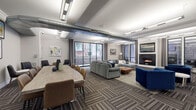 Located at 121 Towne St in Stamford, CT, this single-floor clubroom is a well-appointed amenity space designed for both relaxation and social gathering. The welcoming entry foyer features a sleek console table and oversized mirror, leading into expansive open areas with patterned carpet tile flooring throughout. Exposed industrial ductwork contrasts elegantly with crown molding details and linear lighting fixtures, creating a modern yet refined aesthetic.

The main lounge is anchored by a generous sectional sofa, coffee table, and a wall-mounted fireplace, with large sliding glass doors that flood the space with natural light and provide views of the outdoor courtyard. A long dining table with mixed seating accommodates group gatherings nearby. The full kitchen is equipped with dark wood cabinetry, granite countertops, a stainless steel French-door refrigerator, and a central island with bar seating — ideal for entertaining.

The game room area features a classic shuffleboard table and leather club chairs, while exposed ductwork and floor-to-ceiling windows lend an urban loft character. A private seating alcove, adorned with soft watercolor artwork and black leather chairs, offers a quieter retreat within the space. Together, these areas create a versatile, stylish environment suited for a range of social and recreational activities.