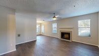 This thoughtfully designed single-floor residence offers a comfortable and functional layout across six distinct spaces. The open living and dining area serves as the heart of the home, showcasing rich dark hardwood flooring, a ceiling fan with light fixture, and a standout tile-surround fireplace flanked by windows that draw in natural light. The dining area is defined by a pendant light fixture and a glass-paned entry door that further brightens the space. The kitchen is well-appointed with dark espresso cabinetry, granite countertops, a subway tile backsplash, and a full suite of stainless steel appliances including a refrigerator, range, and microwave. A dedicated closet provides convenient storage. The spacious bedroom features plush carpeting, a ceiling fan, and a sliding glass door that opens to an outdoor balcony with views of surrounding greenery. The full bathroom is finished with large-format gray wall tiles, a granite-topped vanity with dark cabinetry, and a soaking tub with shower. Throughout the residence, a neutral color palette and textured ceilings create a clean, cohesive aesthetic.