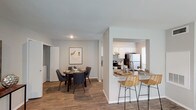 This two-floor residence offers a well-organized layout with thoughtfully designed spaces across both levels. The living room serves as a standout feature, boasting dramatically high ceilings that amplify the sense of openness, large windows that invite natural light, and a tile-surround fireplace that anchors the room as a focal point. Wood-style flooring runs throughout the main living areas, adding warmth and continuity.

The galley-style kitchen is efficiently designed with white cabinetry, granite countertops, stainless steel appliances including a refrigerator, range, and dishwasher, and a bright window at the far end. A peninsula with bar seating connects the kitchen to the dining area, which comfortably accommodates a four-person table. Notably, the dining space includes a closeted in-unit washer and dryer for added convenience.

The bedroom is carpeted and generously sized, with a ceiling fan and direct access to a well-appointed bathroom featuring a dual-sink granite vanity, wood-style flooring, and a large mirror with overhead lighting. A spacious walk-in closet with dual hanging rods and carpet flooring provides ample storage. The entry area also features carpet and a chair rail detail along the walls.