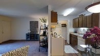 This single-floor residence showcases a practical and inviting layout designed to maximize everyday comfort. The kitchen is well-appointed with dark wood cabinetry, a white refrigerator, and a range, providing ample storage and workspace. A hardwood-style floor grounds the kitchen area, complemented by a flush-mount fluorescent light fixture that ensures bright, functional illumination. A central dividing wall with a pass-through design separates the kitchen from the adjoining living space, creating a sense of defined zones while maintaining an open feel. The living area features plush carpeting in a warm, neutral tone, lending a cozy ambiance to the space. A decorative black ladder shelf serves as a focal point, styled with greenery, decorative objects, and framed accents. A teal sideboard cabinet with glass doors adds a pop of color and additional storage. Decorative wall panels contribute an artistic touch to the living space. Natural and artificial lighting work together to create a warm, welcoming atmosphere throughout. The overall design balances functionality with homey charm, making it a comfortable single-level living space.