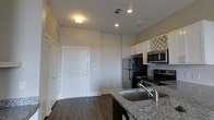 Located at 515 Montgomery St in the heart of Savannah, Georgia, this single-floor residence offers a well-designed layout with contemporary finishes throughout. The kitchen serves as a focal point of the space, showcasing granite countertops, a stainless steel sink, and a full suite of stainless steel appliances including a refrigerator, electric range, and over-the-range microwave. White cabinetry with decorative lattice accents provides ample storage, lending the kitchen a clean and classic aesthetic. Dark hardwood flooring runs throughout the space, creating a warm contrast against the light-toned walls and white trim. Recessed lighting and ceiling-mounted fixtures ensure the interior is well-lit, while elevated ceilings contribute to an open, airy feel. The entryway features a paneled white door with a closet nearby, offering practical storage from the moment you step inside. The neutral color palette and modern finishes create a cohesive and inviting atmosphere throughout the unit. The overall design balances functionality with style, making this Savannah property a comfortable and attractive living space in a prime urban location.
