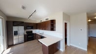 Located at 6653 Lookout Rd in Boulder, Colorado, this single-floor unit presents a contemporary design with a cohesive neutral palette throughout. The kitchen serves as a focal point of the space, featuring rich dark-wood cabinetry with sleek hardware, light quartz countertops, and a full suite of black appliances including a range, over-the-range microwave, dishwasher, and stainless steel refrigerator. A built-in wine rack adds a distinctive touch above the refrigerator, while open corner shelving provides additional display and storage. Track lighting illuminates the kitchen, and a peninsula counter extends the workspace, offering casual seating potential. Light wood-style flooring runs through the main living and kitchen areas, contributing to a clean, modern aesthetic. The living area is generously proportioned with neutral gray walls and large windows that allow natural light to filter in. The bedroom is carpeted for comfort and includes a spacious walk-in closet with wire shelving on both sides. The bathroom is well-equipped with a full tub and shower combination, built-in open shelving, a dark-wood vanity with a light countertop, and a large mirror.