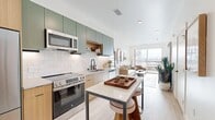 Located at 634 S 400 W in Salt Lake City, Utah, this thoughtfully designed one-bedroom, one-bathroom residence offers a modern, efficient layout across a single floor. The open-concept kitchen and living area serves as the heart of the home, where sage green upper cabinetry pairs with warm wood lower cabinets and a white tile backsplash. Stainless steel appliances — including a refrigerator, electric range, microwave, and dishwasher — complement the clean quartz countertops. A freestanding island with bar seating adds both function and style to the space. Light wood-tone flooring runs throughout, lending warmth and continuity to every room. The living area is bright and airy, anchored by a large sliding glass door that opens to a private balcony with urban views of the Salt Lake City skyline. The bedroom is a comfortable retreat with a generous window that draws in natural light, direct access to a walk-in closet, and a secondary closet for additional storage. The bathroom features warm wood vanity cabinetry, an arched mirror with matte black hardware, open shelving, and tile-surround tub/shower. Clean white walls and recessed lighting throughout give the entire residence a crisp, contemporary feel.
