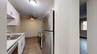 Located in Coon Rapids, Minnesota, this single-floor unit offers four bedrooms and one bathroom within a practical and efficiently designed layout. The galley-style kitchen is a standout feature, outfitted with white shaker cabinets, light stone countertops, stainless steel appliances including a refrigerator, electric range, and over-the-range microwave, and durable light wood-style flooring. The living room is spacious and open, featuring rich dark hardwood-style flooring, a ceiling fan, and large windows that allow generous natural light to fill the room. A second living area or flex space also features the same flooring and ceiling fan, offering versatile functionality. The four bedrooms are finished with plush gray carpeting and feature windows overlooking the outdoors, with baseboard heating units running along the walls. The neutral, light gray tones throughout the bedrooms create a calm and restful atmosphere. The bathroom includes a clean, white soaking tub and shower combination. A connecting hallway ties the rooms together efficiently. Overall, the unit presents a clean, updated aesthetic with consistent finishes and practical amenities throughout.