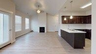 This single-floor residence offers a thoughtfully designed layout that balances functionality with modern aesthetics. Light hardwood-style flooring flows seamlessly throughout the space, creating a cohesive and inviting atmosphere.

The kitchen is a standout feature, outfitted with rich dark espresso cabinetry, crisp white countertops, and a full suite of stainless steel appliances including a range, over-the-range microwave, dishwasher, and refrigerator. A kitchen peninsula with pendant lighting and an integrated sink serves as both a practical workspace and a natural divider between the kitchen and the living area.

The living area is bright and airy, benefiting from multiple windows dressed with horizontal blinds that allow ample natural light. Vaulted ceilings with track lighting add vertical dimension and an open feel, while a direct-access exterior door provides convenient entry.

The bathroom is clean and well-appointed, featuring a vanity with dark cabinetry and white countertop, a tiled tub-shower combination, and durable flooring consistent with the rest of the home.

A dedicated laundry room houses a stacked washer and dryer unit alongside an electrical panel, maximizing utility in a compact footprint. The overall design emphasizes clean lines, neutral tones, and practical finishes throughout.