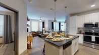 This well-appointed single-floor residence offers a thoughtfully designed open-concept layout that seamlessly connects the kitchen, living, and dining areas. The kitchen serves as a centerpiece, featuring white shaker cabinetry, dark granite countertops, stainless steel appliances including a French door refrigerator, a subway tile backsplash, and a large island with bar seating illuminated by industrial-style pendant lights. Wood-look flooring flows throughout the main living areas, adding warmth and continuity to the space.

The living room is generously sized, bathed in natural light through multiple large windows dressed with dark grommet curtains and wood blinds. A ceiling fan anchors the room, which comfortably accommodates a full seating arrangement. Adjacent to the living area, a cozy dining nook features corner windows on two walls and a pendant light overhead, creating an intimate yet bright setting.

Both bedrooms are carpeted and well-proportioned, each outfitted with ceiling fans and large windows that invite natural light. The primary bedroom connects to a walk-in closet with built-in shelving, which leads directly into a full bathroom featuring a tiled tub-shower combination and wood-look tile flooring. A second full bathroom mirrors this clean, modern aesthetic. Throughout the space, neutral tones and contemporary finishes create a cohesive and inviting ambiance.