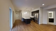 Located at 36 Pine St in Poughkeepsie, NY, this thoughtfully designed 3-bedroom, 2-bathroom residence offers a well-appointed single-floor layout with modern finishes throughout. The open-concept kitchen and living area serves as the heart of the home, featuring rich hardwood-style flooring that adds warmth and continuity across the space. The kitchen is equipped with sleek dark cabinetry, stainless steel appliances including a French door refrigerator, electric range, and microwave, all complemented by a central island with a white countertop and integrated sink. Stylish pendant lighting hangs above the island, enhancing the contemporary aesthetic alongside recessed ceiling lights that provide bright, even illumination. The clean white walls and smooth ceilings contribute to an airy, open ambiance throughout. A hallway connects the main living area to the three bedrooms and two bathrooms, offering a logical and functional floor plan. The combination of modern design elements, quality appliances, and durable flooring makes this residence a well-rounded and move-in-ready home in the heart of Poughkeepsie.