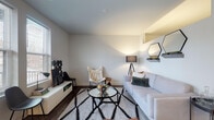 Located at 122 Parsons Ave in Columbus, Ohio, this thoughtfully designed single-floor residence blends modern aesthetics with functional living. The living area sets a welcoming tone with dark hardwood flooring, neutral walls, and abundant natural light streaming through large windows. A built-in wall shelf adds a decorative touch, while the open layout creates a comfortable, airy feel.

The kitchen is a standout feature, outfitted with crisp white shaker cabinetry, stainless steel appliances including a refrigerator, range, microwave, and dishwasher, and a classic white subway tile backsplash that extends floor to ceiling. Track lighting illuminates the space, and a compact dining area provides a convenient spot for casual meals.

The bedroom offers a calm retreat with soft carpeting, a wall-mounted desk, and a sliding closet with built-in shelving. A clerestory-style window allows natural light to filter in while maintaining privacy. The space is well-proportioned and versatile.

The bathroom is finished with large-format gray floor tiles, a white subway tile walk-in shower, a white vanity with a clean-lined countertop, and matte black fixtures that lend a contemporary edge. A direct exterior door off the living space provides convenient outdoor access, with views of the surrounding Columbus neighborhood.
