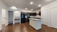 Located at Marbach Oaks in San Antonio, Texas, this single-floor residence offers a well-designed layout with a clean, contemporary aesthetic throughout. Rich, dark wood-look flooring runs seamlessly across the living, dining, and kitchen areas, creating a cohesive and polished look.

The open-concept kitchen is a standout feature, equipped with dark espresso cabinetry, granite-style countertops, black appliances including a refrigerator, range, and microwave, and a central island that provides additional prep and seating space. Recessed lighting and a pendant light illuminate the kitchen, while a built-in arched nook with shelving adds a charming architectural detail.

The living area is bright and welcoming, benefiting from natural light through multiple windows with blinds and a glass door. A ceiling fan with a light fixture adds comfort and functionality to the space.

The bedrooms continue the wood-look flooring and feature ceiling fans, generous closet space, and access to well-appointed bathrooms. The bathrooms include dark vanity cabinetry with granite countertops, large mirrors, and clean white tile surrounding the soaking tub and shower combination.

Throughout the unit, white walls and crisp trim provide a neutral backdrop, making each space feel open, airy, and move-in ready.