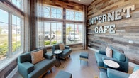 This single-floor amenity space in Davenport, Florida, is thoughtfully designed to serve as a multifunctional community hub. The internet café lounge greets visitors with soaring ceilings, floor-to-ceiling windows framed by sheer curtains, and abundant natural light. Reclaimed wood-panel accent walls lend a warm, rustic character, while teal upholstered seating and a circular accent table create an inviting social atmosphere.

The full-length kitchen is a standout feature, outfitted with expansive white quartz countertops, dark cabinetry, a mosaic tile backsplash, stainless steel appliances, a microwave, and a coffee station. Pendant globe lighting adds a refined touch, and a breakfast bar with bar stools offers casual seating.

A dedicated workstation area provides a long built-in desk with computer access, a tufted banquette, and sculptural wall décor, ideal for productivity. Geometric mirror panels and contemporary artwork enhance the visual interest of the space.

The conference room features a coffered ceiling, a statement cluster pendant light fixture, a large glass conference table surrounded by white leather chairs, and views to the outdoors through sheer-draped windows. Together, these areas create a polished, versatile space suited for work, collaboration, and relaxation.