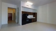 This single-floor space features an open layout that seamlessly integrates the kitchen with the surrounding living area. The kitchen is outfitted with rich, dark wood cabinetry that extends from floor to ceiling, providing generous storage space. Black appliances, including a full-size refrigerator, a range with an overhead microwave, and a dishwasher, are fitted neatly beneath the cabinetry. A double-basin sink with a single-handle faucet is positioned along the countertop, which features a clean, light-colored surface that contrasts effectively with the dark cabinetry. Overhead, a fluorescent light fixture illuminates the kitchen workspace, while a ceiling vent ensures proper climate control. The flooring throughout is a light-toned vinyl, offering a neutral foundation that complements the overall color palette of the space. The walls are finished in a crisp white, contributing to a clean and modern aesthetic. A hallway visible from the kitchen leads to additional areas of the unit, hinting at further functional spaces beyond. The layout is straightforward and efficiently designed, maximizing usability within a compact footprint.