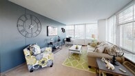 Located on S Dr Martin Luther King Jr Dr in Chicago's Bronzeville neighborhood, this single-floor residence offers a well-organized layout with two bedrooms, a living room, kitchen, and full bathroom. The floor plan reveals a logical flow between spaces, with rooms positioned to maximize functionality and comfort.

The living room serves as the centerpiece of the unit, featuring a broad bank of windows fitted with horizontal blinds that invite substantial natural light and offer views of the surrounding tree-lined landscape. Neutral carpet, a cool blue accent wall, and ceiling fan lighting contribute to a relaxed yet stylish atmosphere.

Both bedrooms are generously proportioned, each equipped with ceiling fans and large windows that provide ample daylight. One bedroom features a tufted upholstered headboard with silver-toned furnishings in a soft, neutral palette, while the second presents a darker, classic sleigh-bed aesthetic with wide windows overlooking the exterior.

The kitchen is outfitted with white cabinetry, dark countertops, a gas range, dishwasher, and tile flooring. A window above the counter further brightens the workspace. The bathroom is clean and efficiently designed, featuring a tub-shower combination, vanity with under-sink storage, and a mirrored medicine cabinet.