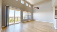 This single-floor residence is defined by its dramatic vaulted ceilings in the main living area, which rise to an impressive height and are lined with transom windows that flood the space with natural light. A ceiling fan with a wood-toned finish hangs centrally, enhancing airflow throughout the open layout. Light wood-look flooring extends across the living area, complementing the neutral gray wall tones and crisp white baseboards.

The living space opens directly to a balcony through a sliding glass door, framed by a large window with horizontal blinds that offers expansive outdoor views. The hallway features a built-in double sliding closet with paneled white doors, providing generous storage.

The kitchen is outfitted with gray shaker-style cabinetry, a quartz-look countertop, a decorative hexagonal tile backsplash, and a full suite of stainless steel appliances including a refrigerator, microwave, and cooktop. The bedrooms transition to plush carpeting and include ceiling fans and windows that bring in natural light. The bathroom features porcelain tile flooring, a marble-look tiled shower surround, gray vanity cabinetry, and chrome fixtures, creating a clean and contemporary aesthetic throughout.