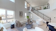 Located in the Koreatown neighborhood of Los Angeles, this contemporary two-story residence showcases a thoughtfully designed open-concept layout with soaring double-height ceilings that create a dramatic sense of space and airiness. Light hardwood flooring flows throughout both levels, complementing the clean white walls and modern aesthetic.

The main living area is anchored by expansive windows that flood the room with natural light and frame views of the surrounding cityscape. A sleek staircase with black metal railings connects the two floors, adding an architectural focal point to the living space. The dining area sits adjacent, completing a seamless entertaining zone.

The kitchen is well-appointed with warm wood cabinetry, crisp white upper cabinets, quartz countertops, a hexagonal tile backsplash, and stainless steel appliances including a range, built-in microwave, and refrigerator. A kitchen island with a double sink adds prep space and functionality.

Bedrooms offer generous proportions, soaring ceilings, and large windows with city views. A spacious walk-in closet with built-in shelving and hanging rods provides ample storage. Bathrooms are finished with large-format floor tiles, vertically stacked white subway tile tub surrounds, wood-accented vanities, white quartz countertops, and backlit mirrors.

The upper level features a versatile lounge area with sweeping views of the Los Angeles skyline.