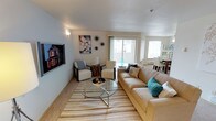 Located at 4720 S Pine St in Tacoma, Washington, Unit 38 is a single-floor residence designed with comfort and functionality in mind. The open-concept living area serves as the heart of the home, featuring large sliding glass doors and generous windows that flood the space with natural light, creating a bright and airy atmosphere throughout the day. The living room is spacious enough to accommodate a full sofa arrangement, accent chairs, and a glass coffee table, all anchored by a striped area rug that adds texture and warmth to the room. A wall-mounted flat-screen television provides a focal point on one side, while decorative wall art adds personality and style to the neutral-toned walls. The layout flows seamlessly into the dining area, which is visible from the living space and benefits from the same abundant natural light. The overall color palette is soft and neutral, with light walls and carpeted flooring contributing to a clean, inviting ambiance. The single-floor plan ensures easy accessibility and a cohesive flow between living spaces. This residence offers a well-balanced combination of open living areas and thoughtful design, making it a comfortable and functional home in the Tacoma community.