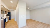 Located at 10999 SE 37th Ave in Portland, Oregon, this efficiently designed one-bedroom, one-bathroom residence offers a thoughtful single-floor layout with clean, contemporary finishes throughout. Light wood-tone flooring runs continuously across all rooms, creating a cohesive and bright aesthetic.

The living room is a welcoming space featuring dual windows that invite natural light and provide views of the surrounding neighborhood. A wall-mounted HVAC unit ensures year-round comfort, while recessed lighting adds a modern touch to the neutral, crisp walls.

The kitchen is well-appointed with warm wood-grain cabinetry extending to the ceiling for ample storage, a full suite of stainless steel appliances including a refrigerator, electric range, microwave, and dishwasher, as well as a single-basin sink. The layout maximizes functionality within a compact footprint.

The bedroom offers a quiet retreat with a large window for natural light, a wall-unit climate control system, and access to a dedicated closet with built-in shelving and a hanging rod. A ceiling fan with integrated lighting enhances comfort in the adjoining space.

The bathroom features modern wood-grain cabinetry, a white quartz countertop, an undermount sink with contemporary fixtures, and a large mirror. The unit also includes in-unit laundry. Clean lines and neutral tones define the overall ambiance of this well-designed residence.