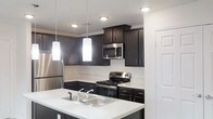 This single-floor residence offers a thoughtfully designed layout with modern finishes throughout. The living area features rich, dark hardwood-style flooring, crisp white walls, and a ceiling fan that enhances comfort and airflow. A glass door opens directly to an outdoor balcony, allowing natural light to fill the space and providing pleasant exterior views.

The kitchen is a standout feature, outfitted with dark espresso cabinetry that extends to the ceiling for ample storage, contrasted by bright white countertops. A peninsula with a double basin sink serves as a functional workspace and casual gathering point. Stainless steel appliances — including a gas range, over-the-range microwave, and full-size refrigerator — complete the modern look. Pendant lighting and recessed fixtures provide layered illumination throughout the kitchen.

The bedroom is finished with plush wall-to-wall carpeting, a ceiling fan, and a large window that brings in generous natural light. A walk-in closet provides practical storage.

The bathroom is generously proportioned, featuring a dual-sink vanity with dark cabinetry and white countertops, a full tub-shower combination, and hardwood-style flooring that ties the space together cohesively. The clean, neutral palette throughout the home creates a bright, welcoming ambiance.