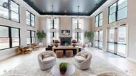Located at 3500 Louis Stephens Dr in Durham, NC, this single-floor clubhouse delivers an impressive blend of modern design and comfortable communal living. The space is organized into two distinct living areas, each offering its own character while maintaining a cohesive aesthetic throughout.

The grand main lounge commands attention with dramatically soaring ceilings accented by a deep navy tray ceiling and statement geometric pendant chandeliers. Floor-to-ceiling black-framed windows flood the room with natural light, while sheer white drapery softens the space. A wood-mantled fireplace serves as a central focal point, flanked by plush seating arrangements and lush potted trees that add organic warmth. French doors open directly to a pool area beyond.

A striking set of black steel-framed sliding barn doors connects the lounge to a second, more relaxed living area. This room features light wood-look tile flooring, oversized framed landscape artwork, and curated seating arranged for casual gatherings.

The entry foyer sets the tone with patterned tile flooring, a sculptural round pedestal table, a circular halo chandelier, and an eclectic full-length mirror. A built-in refreshment bar with marble backsplash, gray cabinetry, and a coffee station is conveniently positioned near the main entrance, completing this well-appointed clubhouse.